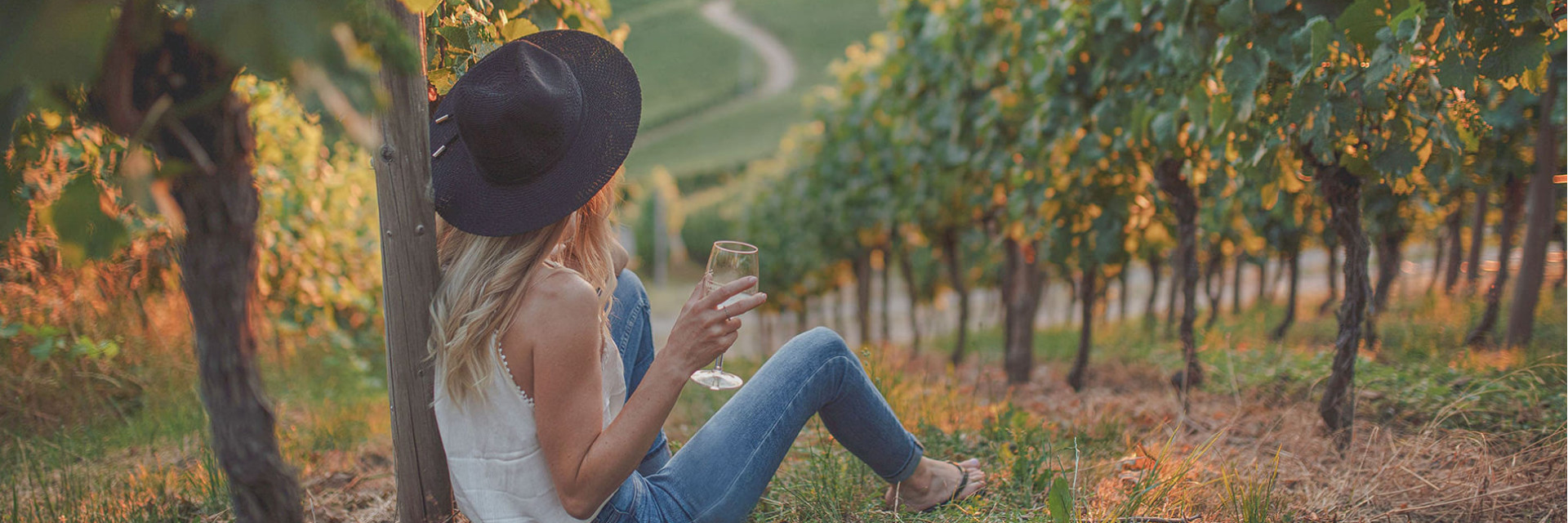 Photo d'une femme dégustant un verre de vin blanc au coucher de soleil sur les vignes.